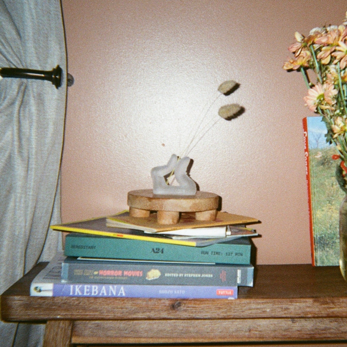 A finger shaped incense holder pinching two pieces of dried bunny tail plant together on a wooden riser on a wooden bench. 