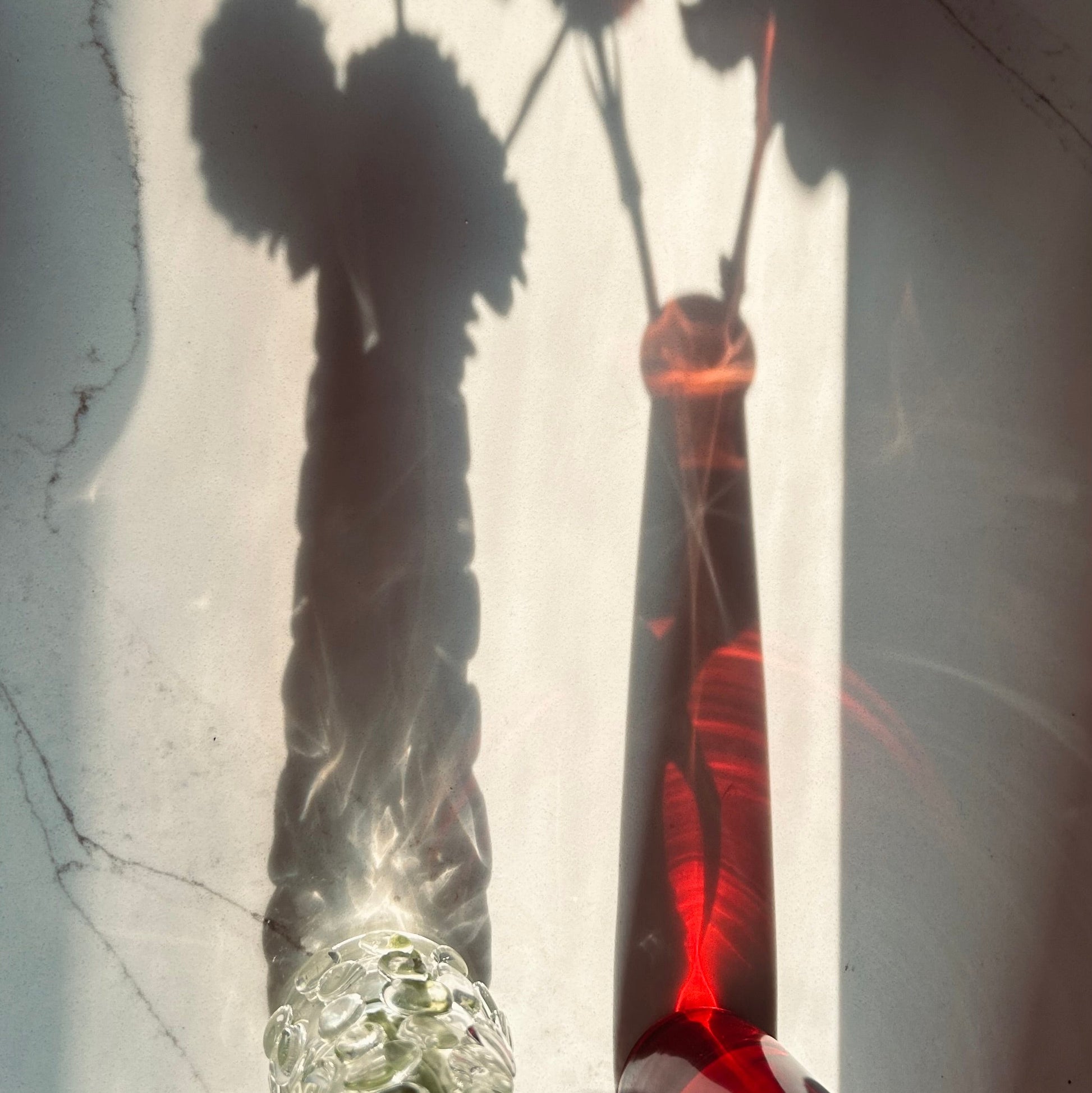 The shadows of light passing through two glass vessels on a white marble countertop. 