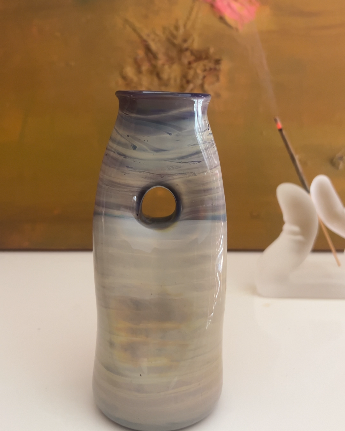 free-form multicolored vessel, colored in muted blues, yellows and purples against a painting. 