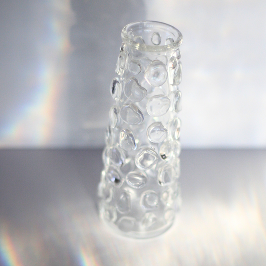 A clear cylinder-shaped glass vessel with clear glass organically shaped orbs all over the vase. The orbs have the appearance of bubbles. 